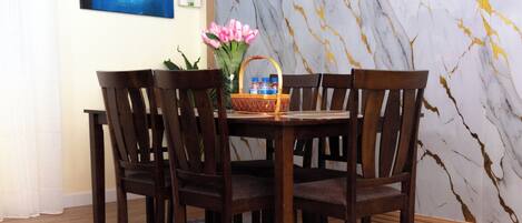 A dining area with a marble wall, wooden chairs, a table, and a vase with flowers.