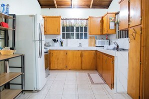 A kitchen with wooden cabinets, a refrigerator, a microwave, and a window with a floral curtain.