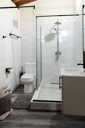 Une salle de bain moderne avec une douche Ă parois de verre, des carreaux de marbre blanc, des toilettes et un lavabo.