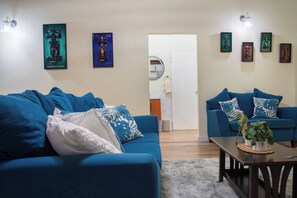 Un salon avec deux canapés bleus, une table basse ornée d’une plante et des œuvres d’art accrochées au mur.