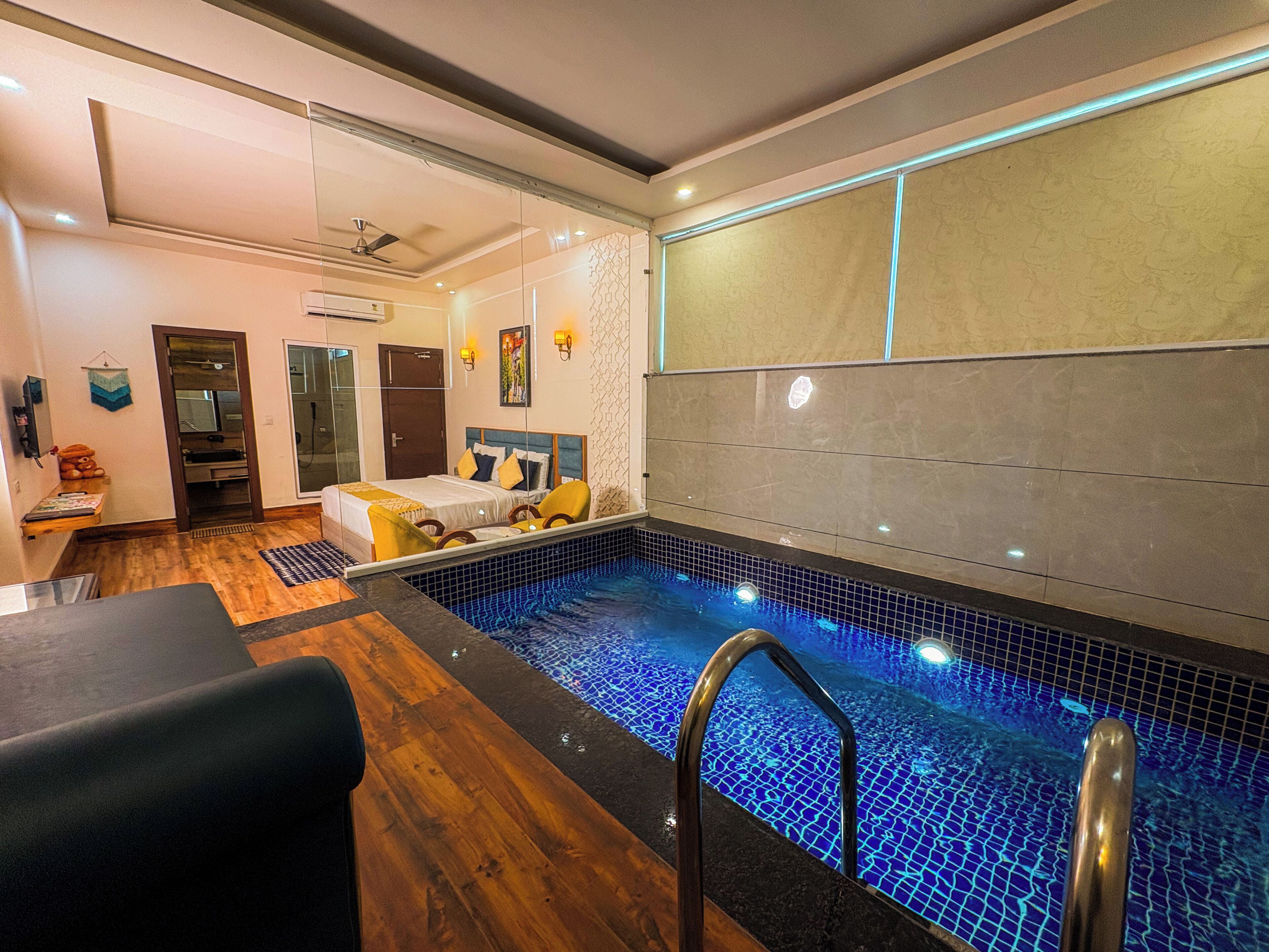 Una habitación de hotel con piscina, una cama con almohadas amarillas y suelo de madera.