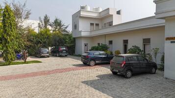 A parking area with several cars, a building with a sign 'Parking at Ooneri Hills,' and a tree-lined street.