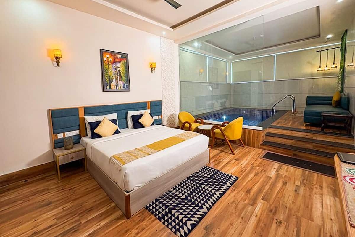 A hotel room with a bed, a small table, a chair, a sofa, a hot tub, and a ceiling fan.
