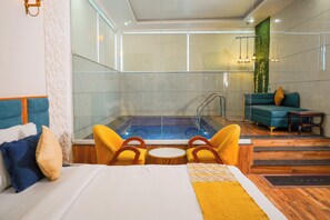Een hotelkamer met een bed, een kleine tafel, twee gele stoelen, een blauwe bank, een houten tafeltje en een whirlpool.