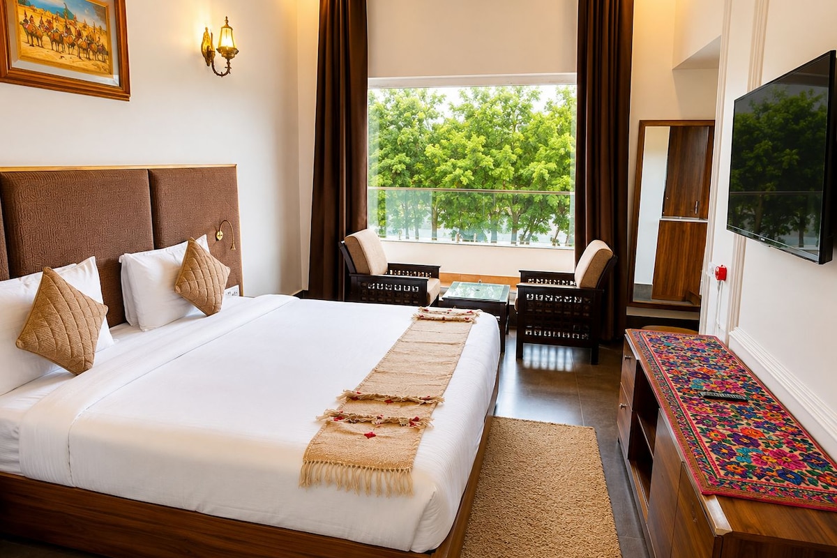 A hotel room with a large bed, a desk, a chair, a TV, and a window with a view of trees.