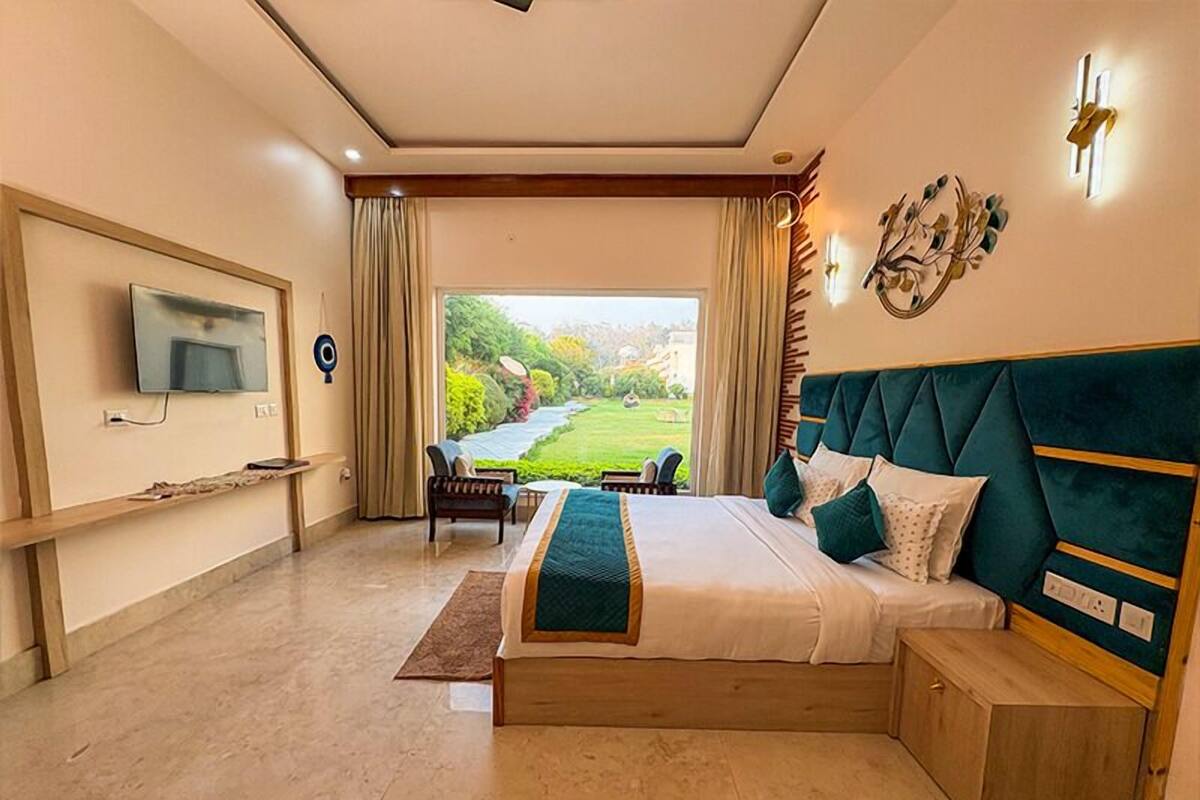 A bedroom with a bed, a TV, a desk, a chair, and a view of a garden.
