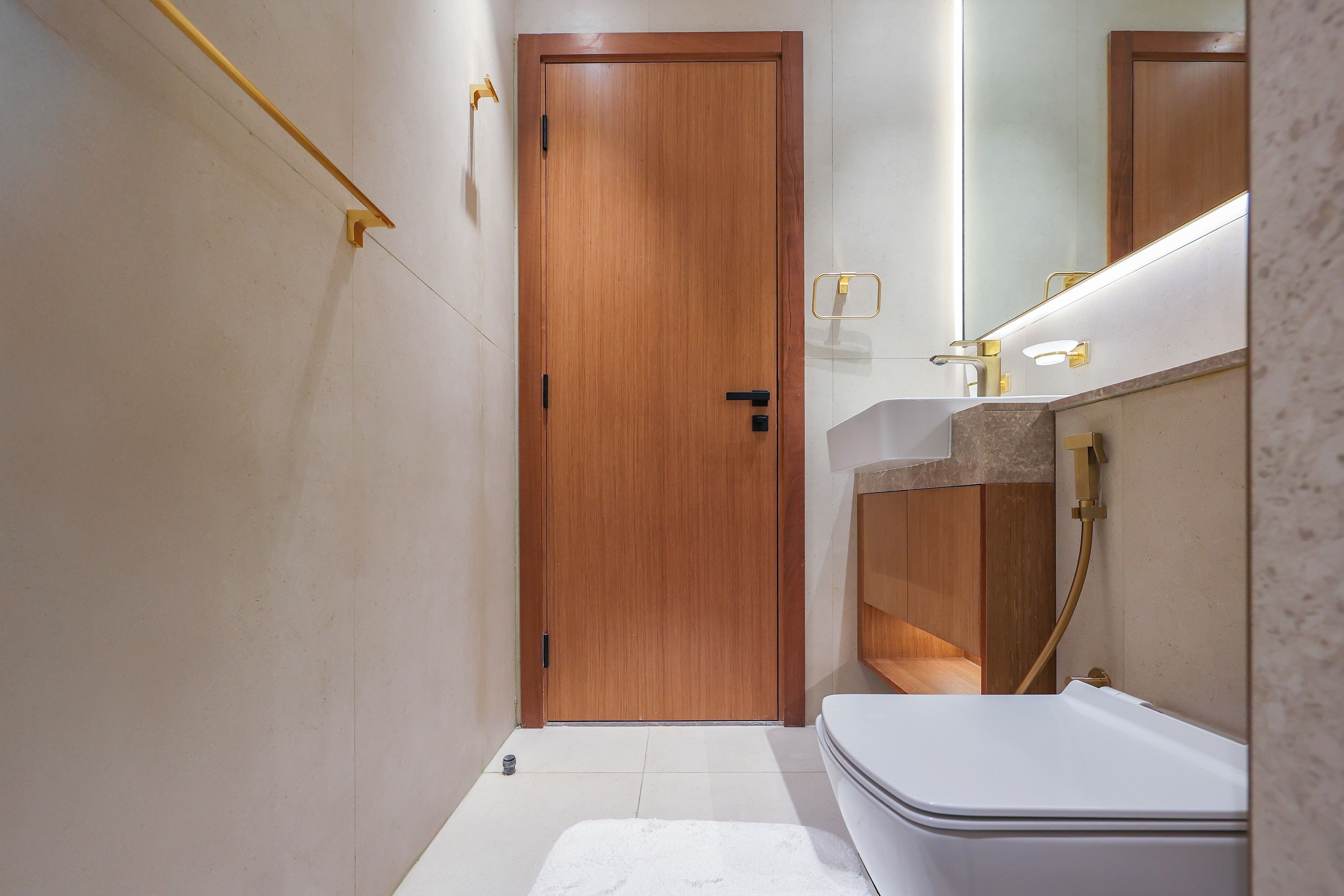 A narrow bathroom with a wooden door, a white sink with a gold faucet, and a white toilet.