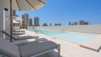 A rooftop pool with lounge chairs and umbrellas, surrounded by high-rise buildings.