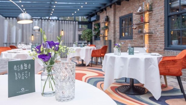 Un área de comedor al aire libre con mesas y sillas, un muro de ladrillo y una sección cubierta con luces colgantes.