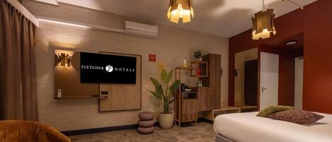 A hotel room with a bed, a TV mounted on the wall, a desk, and a chair.
