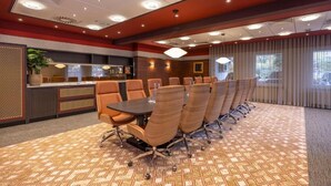 Un salón de conferencias con una larga mesa y múltiples sillas, un área de recepción con mostrador y una alfombra estampada.