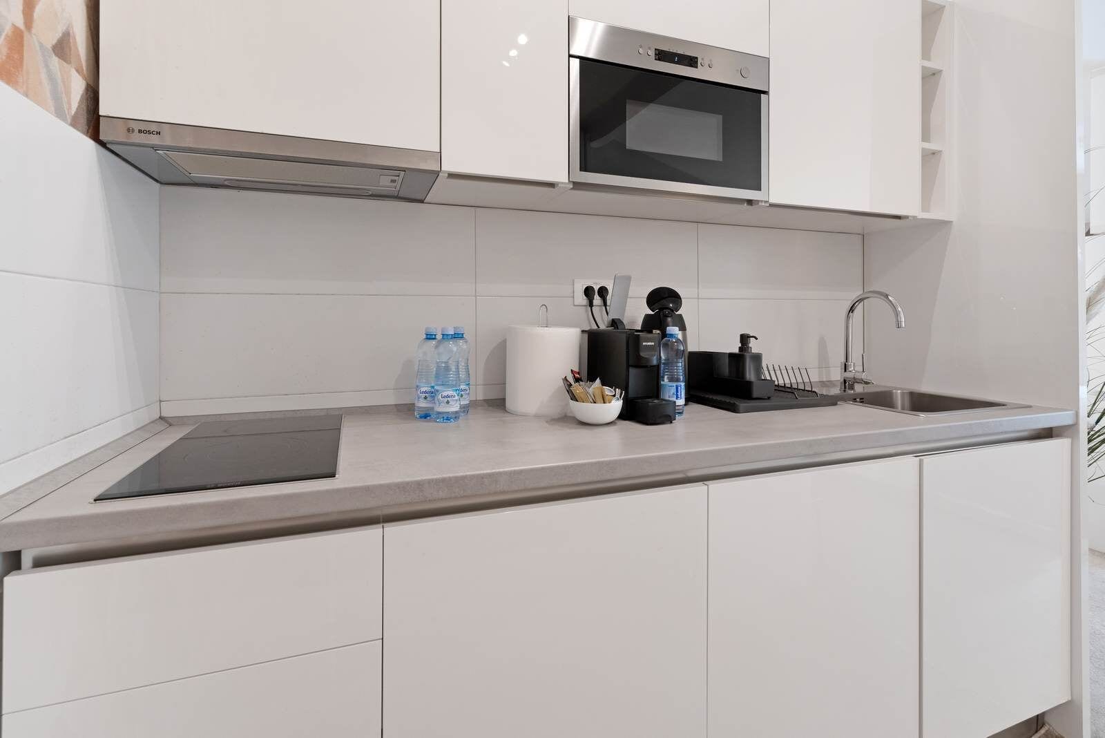 A modern kitchen with white cabinets, a Bosch microwave, a sink, and a countertop with water bottles and kitchen tools.