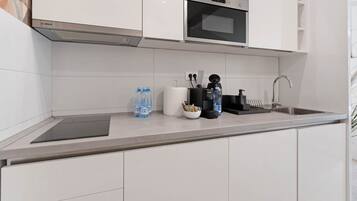 A modern kitchen with white cabinets, a Bosch microwave, a sink, and a countertop with water bottles and kitchen tools.