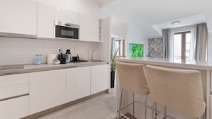 Une cuisine moderne avec des meubles blancs, un four en acier inoxydable et un coin bar équipé de deux chaises rembourrées.