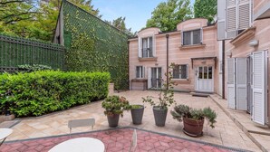 Une cour avec un bâtiment en briques, une haie verdoyante et des plantes en pot.