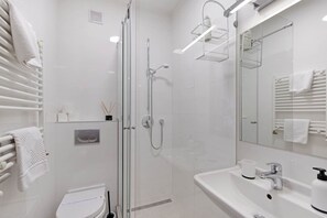 Egy modern fürőszoba üvegfalas zuhanyzóval, fehér mosdókagylóval és WC-vel.