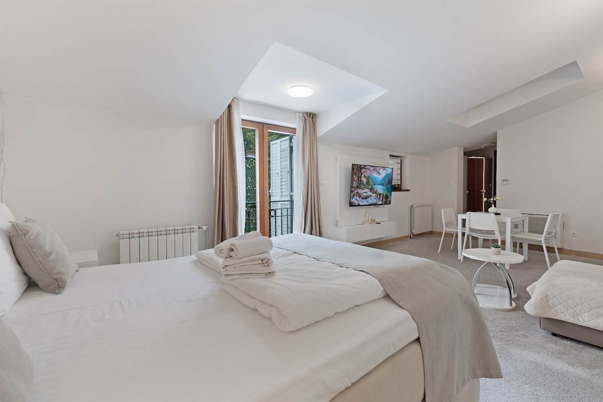 Ein modernes Hotelzimmer mit einem großen Bett, einem Schreibtisch, einem Fernseher und einem Balkon mit Vorhängen.