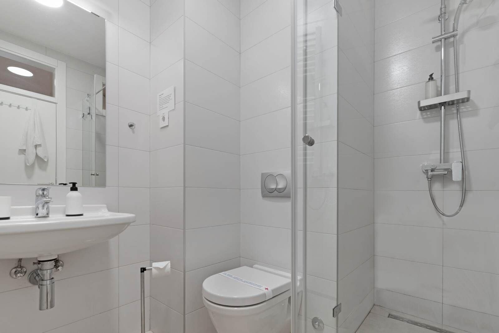 A modern bathroom with a glass-enclosed shower, a white sink with a soap dispenser, and a toilet.