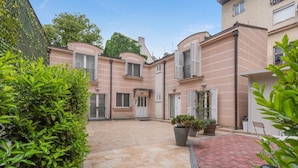 Une cour avec un chemin pavé, des plantes en pot et un bâtiment doté de nombreuses fenêtres et de volets.