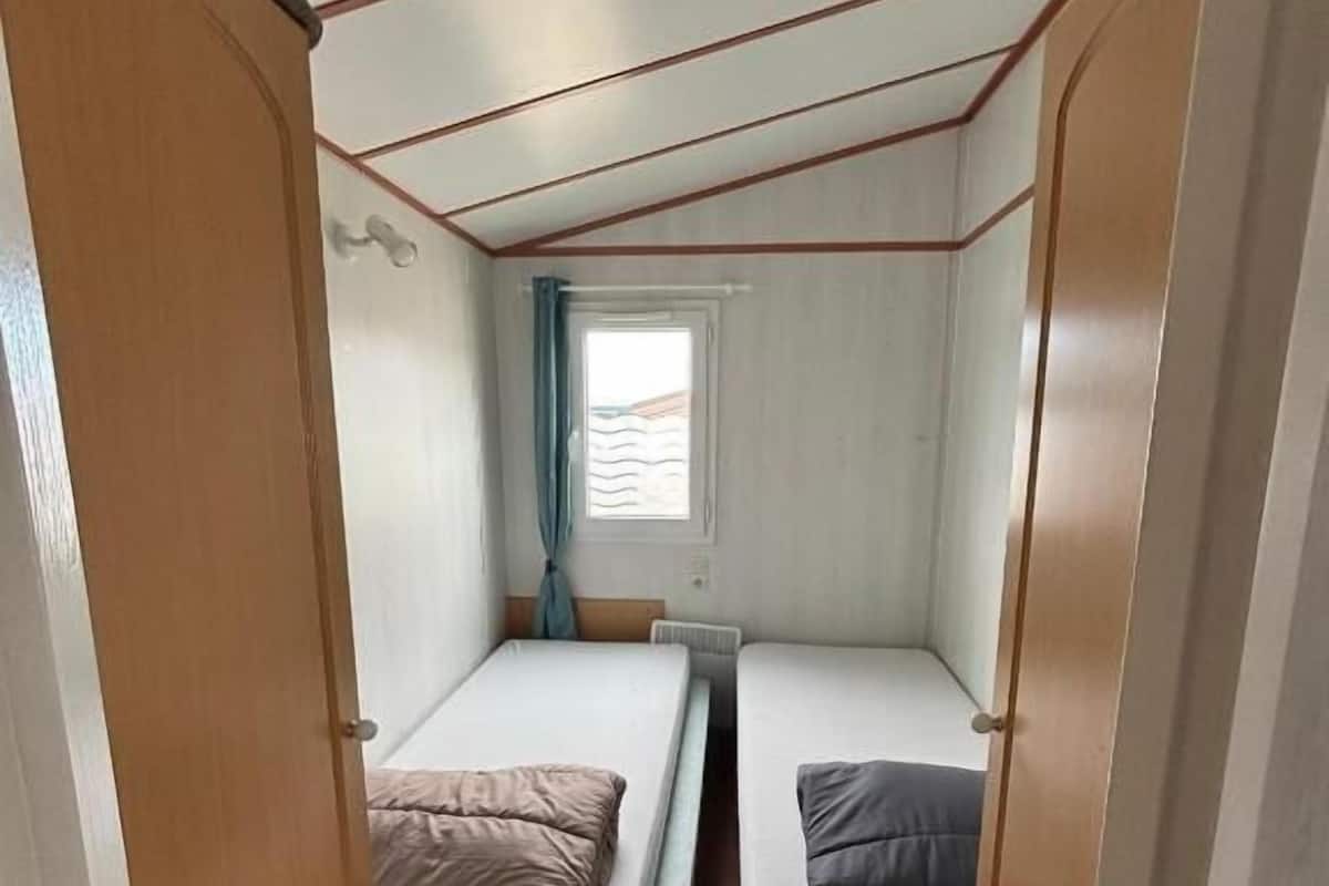 A compact room with two single beds, a window with curtains, and a wooden door.