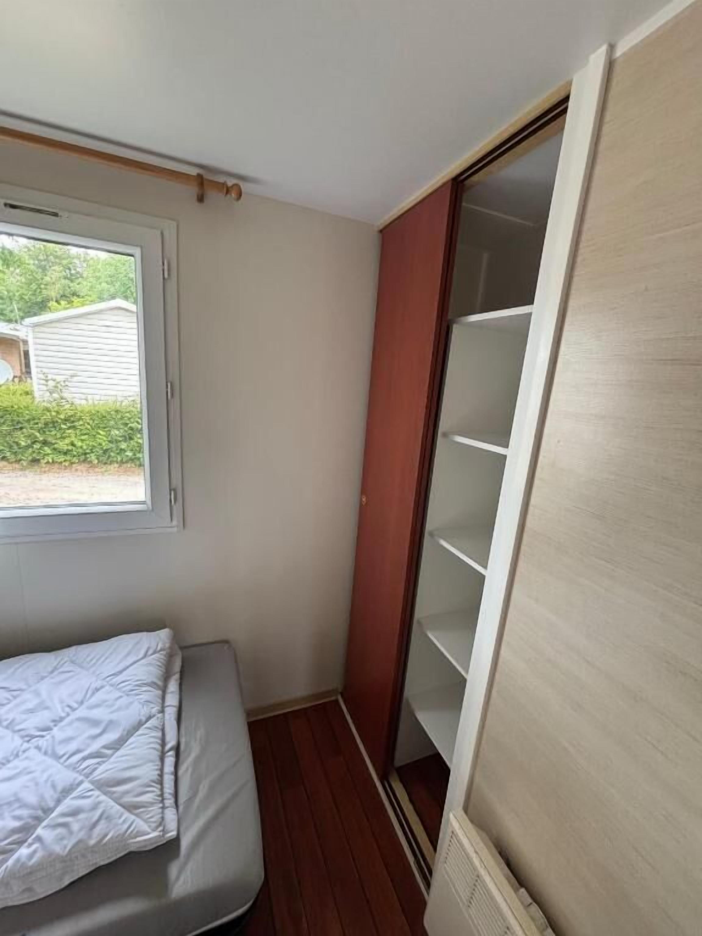 Een kleine kamer met een bed, een schuifdeurkast en een raam.