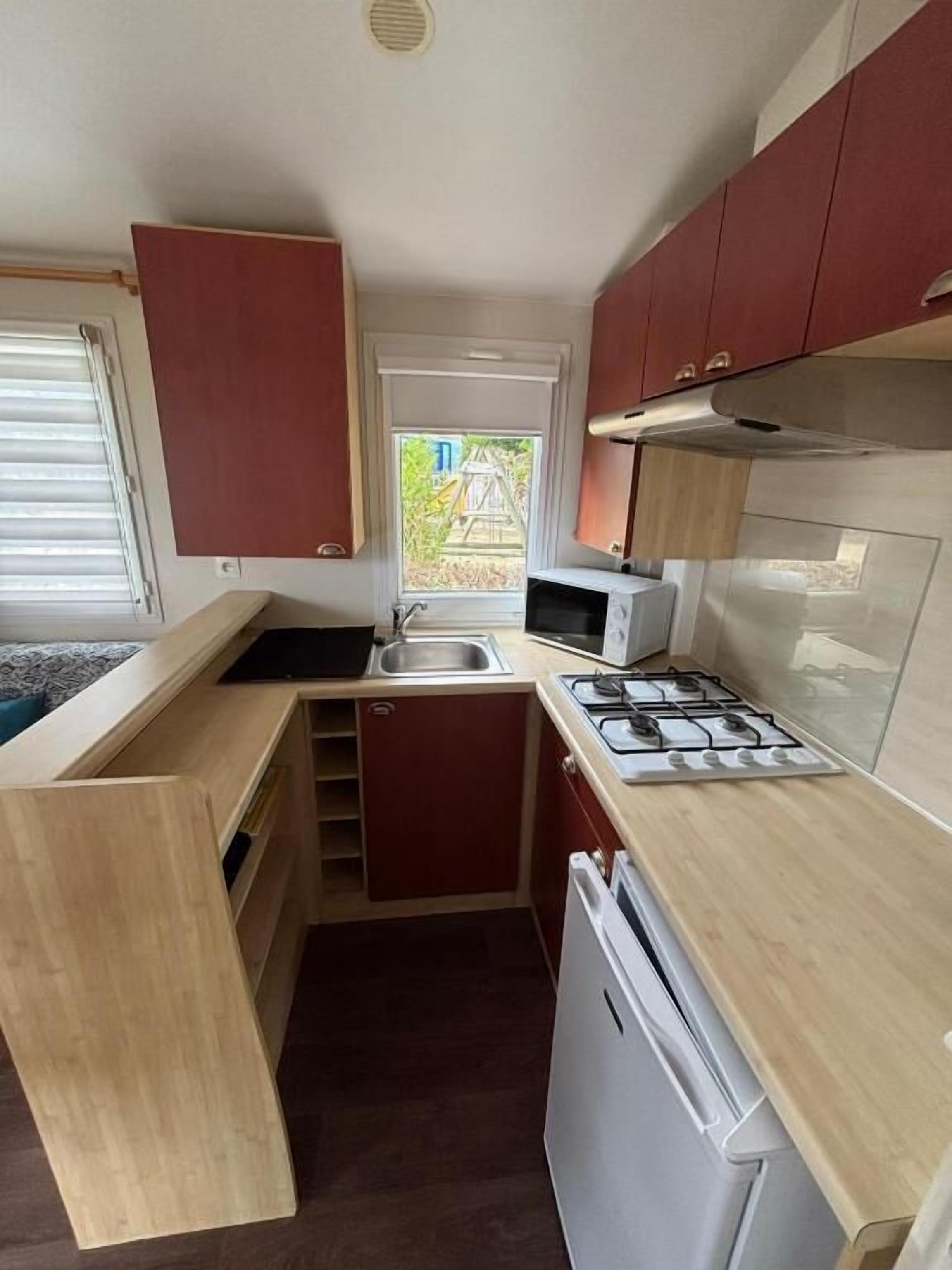 Een kleine keuken met een spoelbak, fornuis, magnetron en houten kastjes.