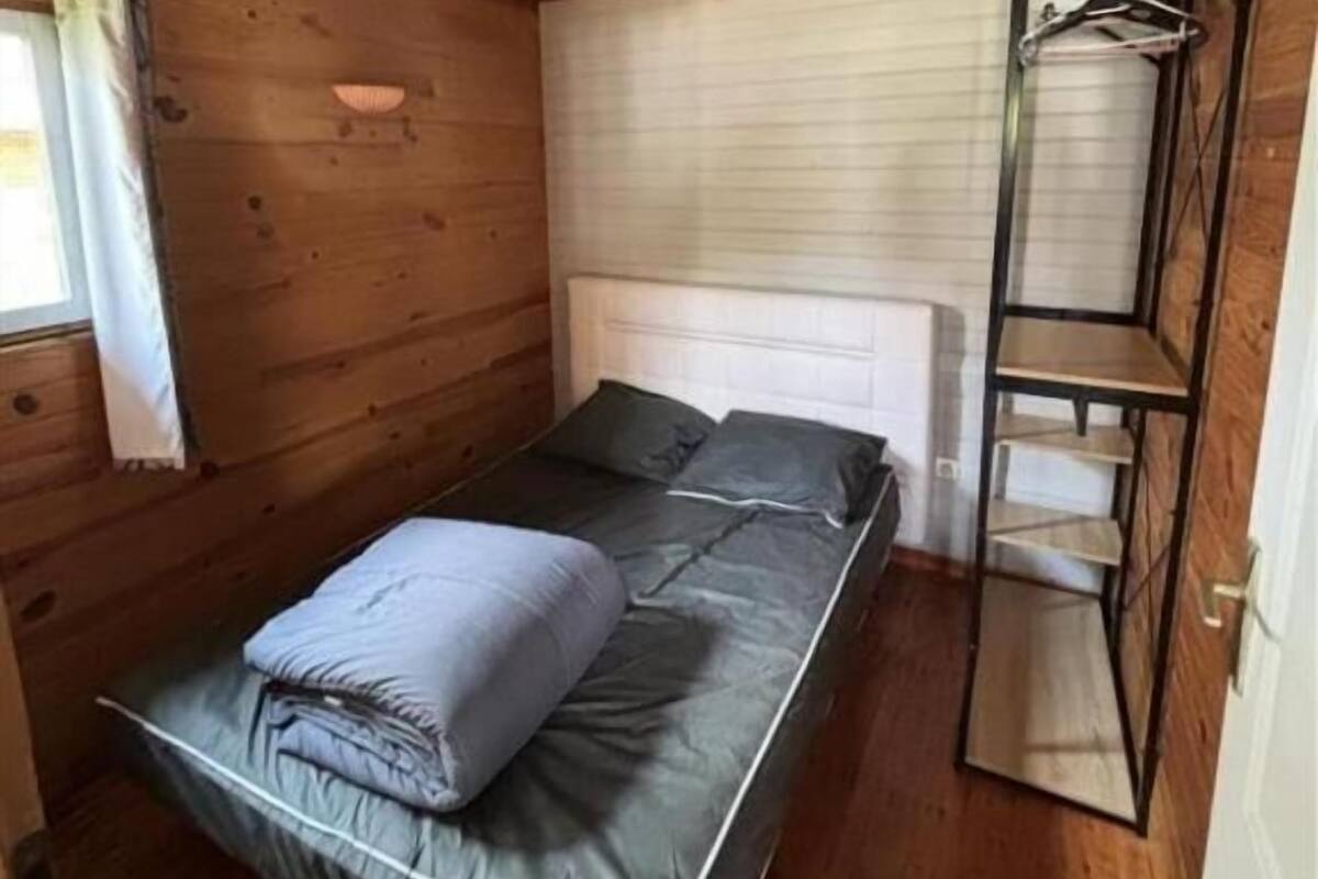 A compact wooden cabin room with a single bed, a small window with curtains, and a built-in wardrobe with shelves.