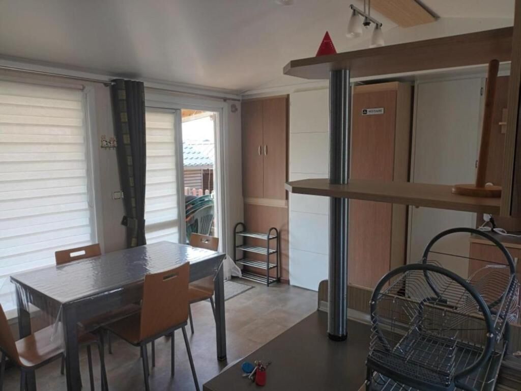 A compact kitchen with a dining table, chairs, a metal rack, and a door with a sign.