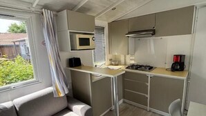 Cozinha compacta com micro-ondas, fogão e máquina de café. Há uma pequena mesa de jantar e um sofá na sala.