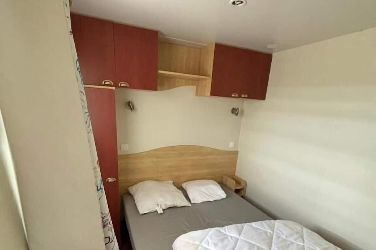 A small, single-bed room with a wooden headboard, a wooden shelf above the bed, and a curtain on the left side.