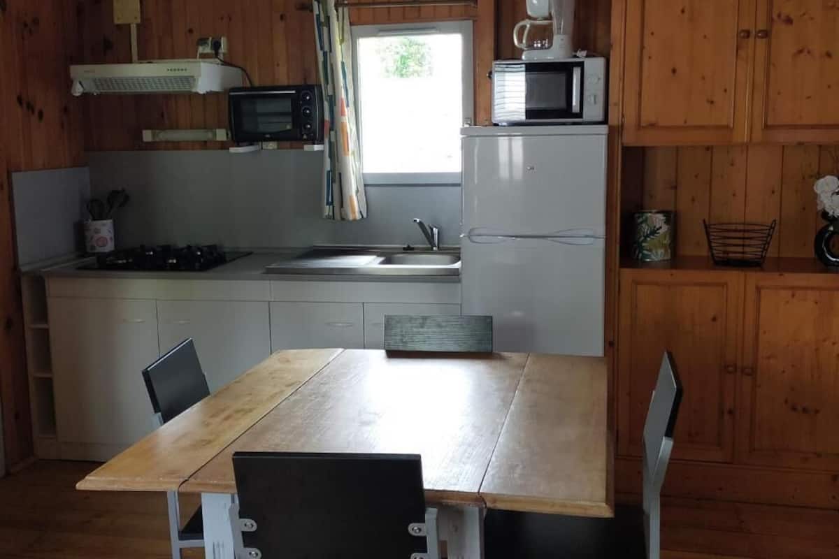 A compact kitchen with wooden cabinets, a microwave, a coffee maker, a sink, and a dining table with chairs.