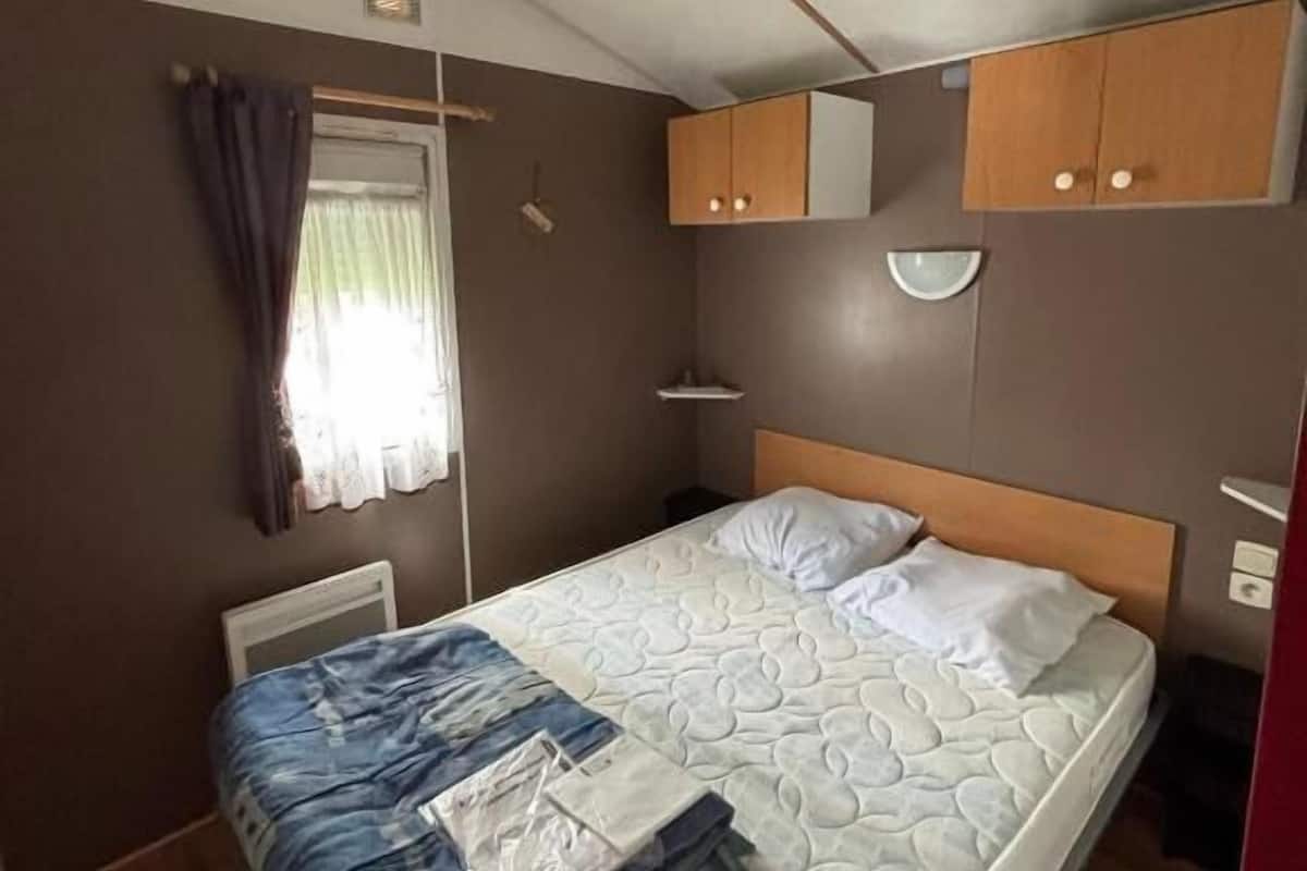 A bedroom with a bed, a window with curtains, a bedside table, and built-in wooden cabinets.
