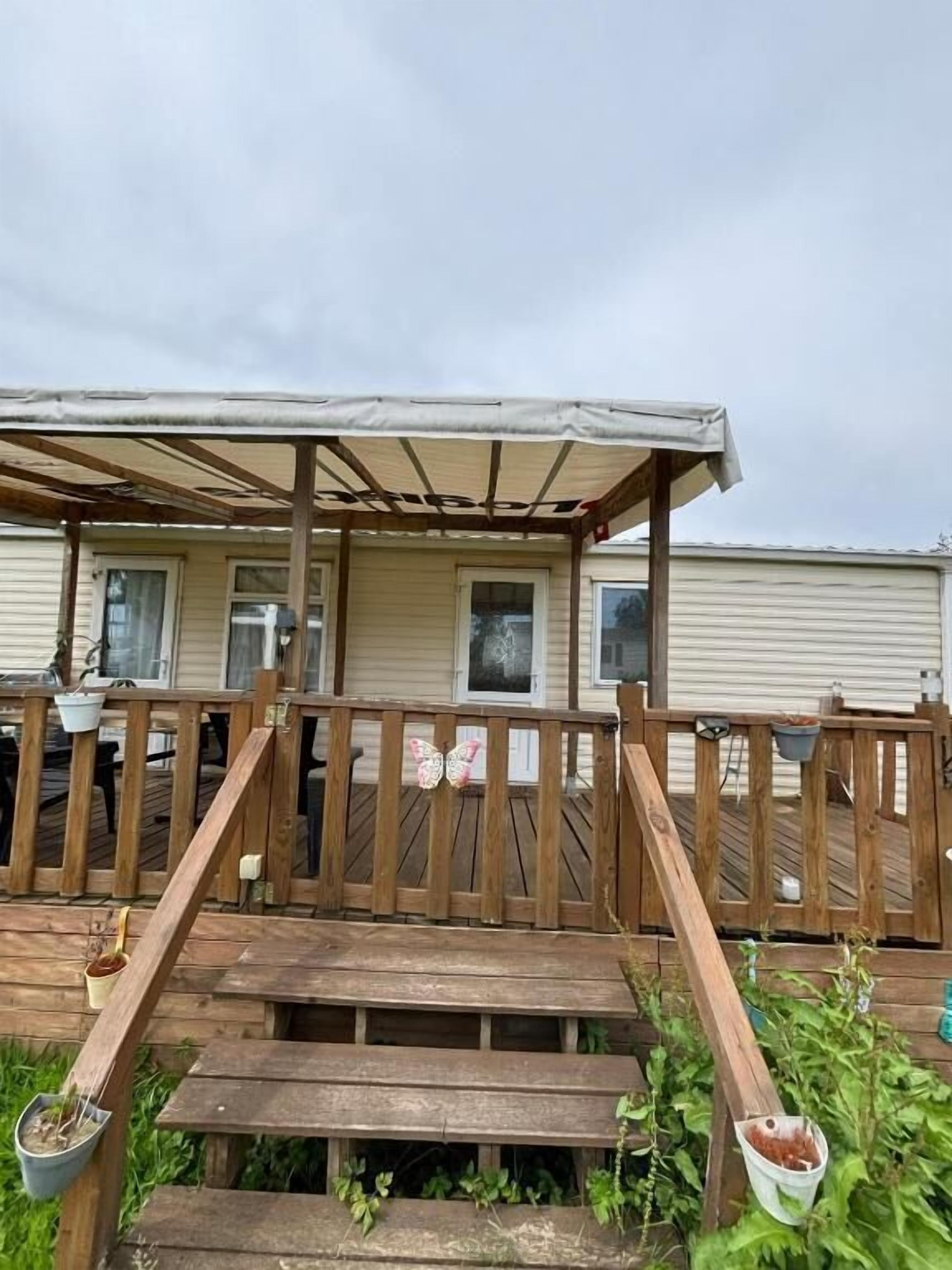 Eine Holzterrasse mit überdachtem Bereich, die zu einem Haus mit Fenstern und einer Tür führt.