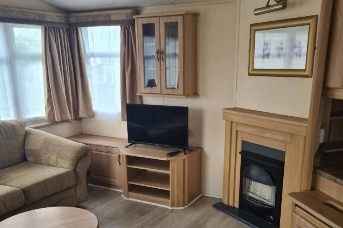 A living room with a sofa, a TV on a wooden stand, a fireplace, and a window with curtains.