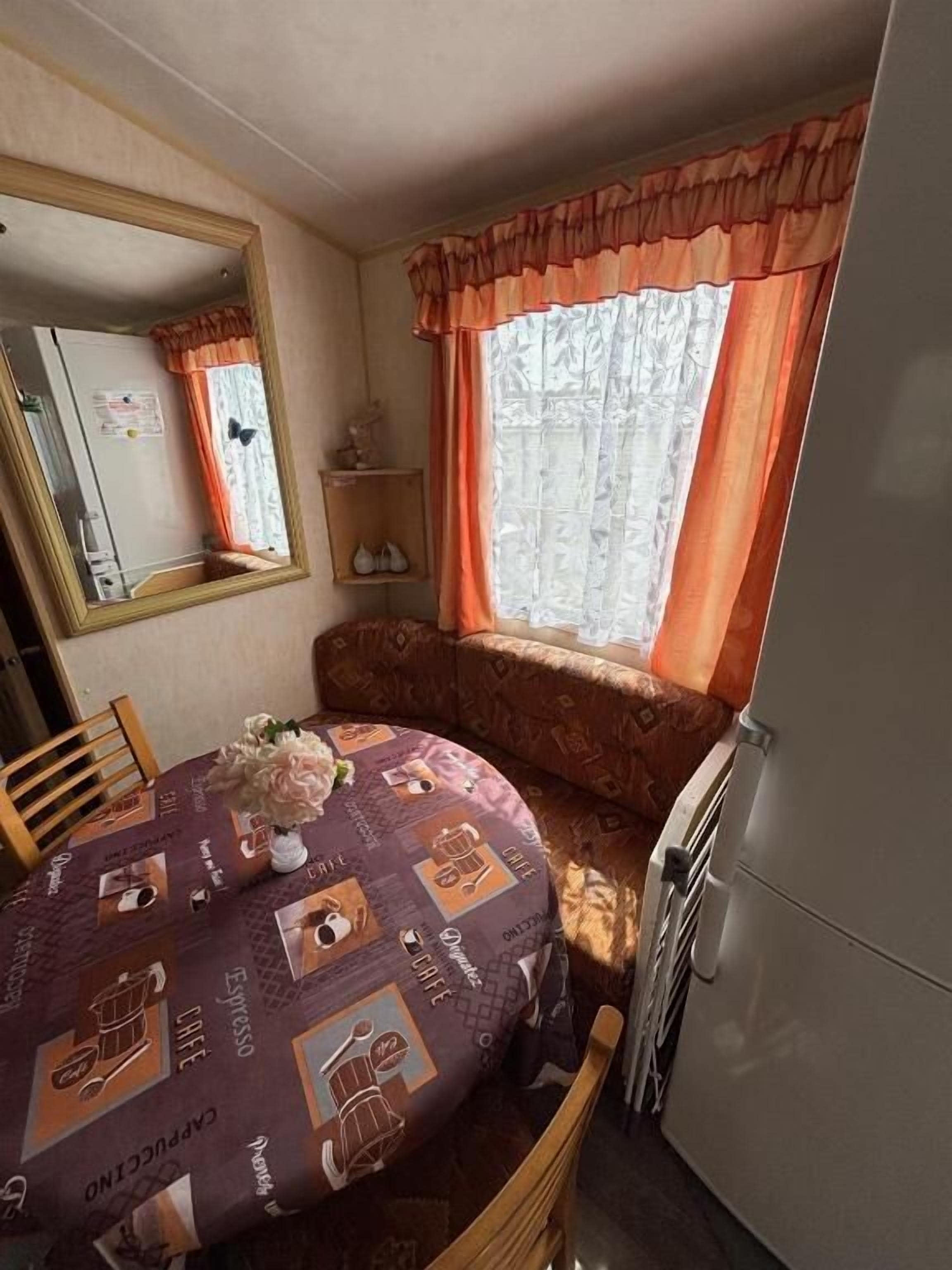 Pieni huone, jossa on pyöreä pöytä, peili, sohva ja ikkuna, jossa on verhot.