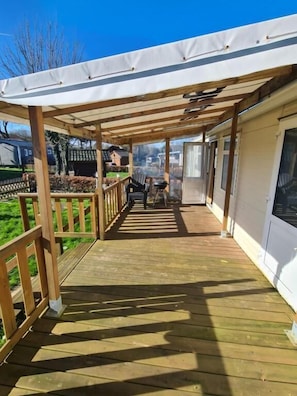 Una terraza cubierta de madera con pérgola, una parrilla y vistas del entorno.
