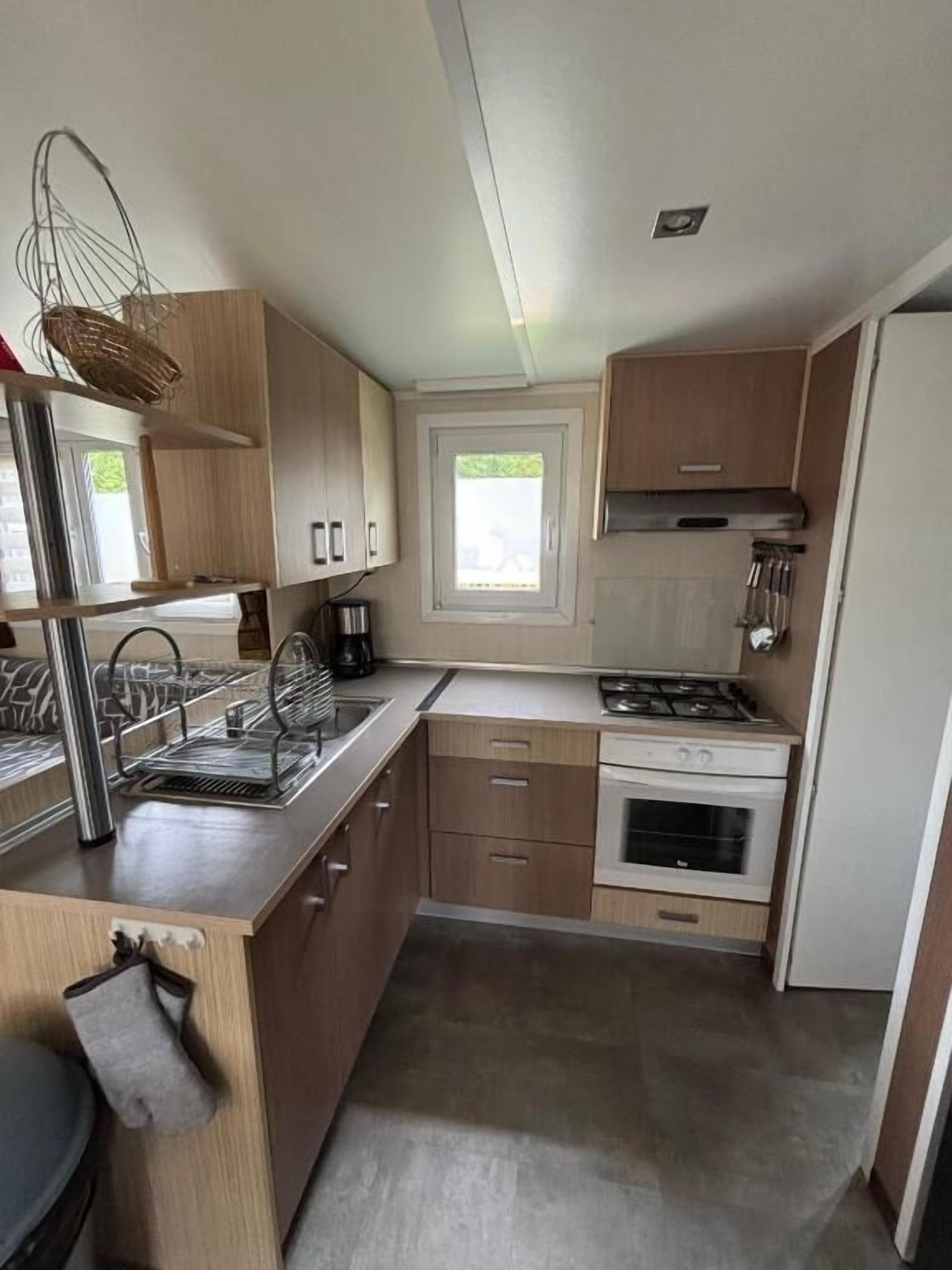 Une cuisine compacte avec des meubles en bois, une cuisinière à gaz, un four encastré et une fenêtre qui laisse entrer la lumière naturelle.