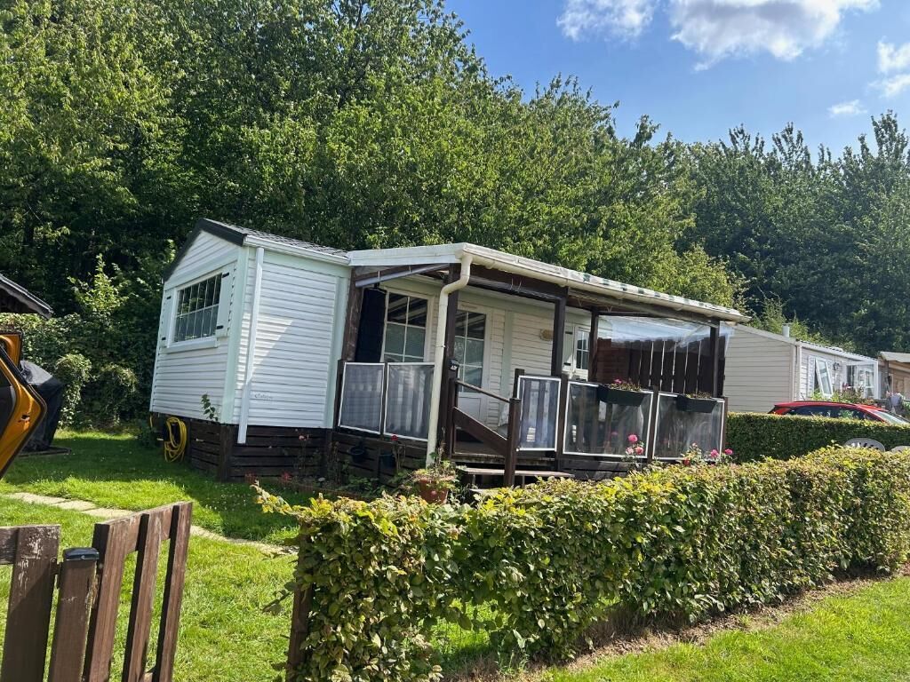 A mobile home with a porch and a covered outdoor area, surrounded by greenery.