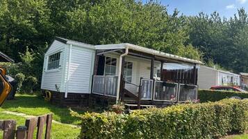 A mobile home with a porch and a covered outdoor area, surrounded by greenery.