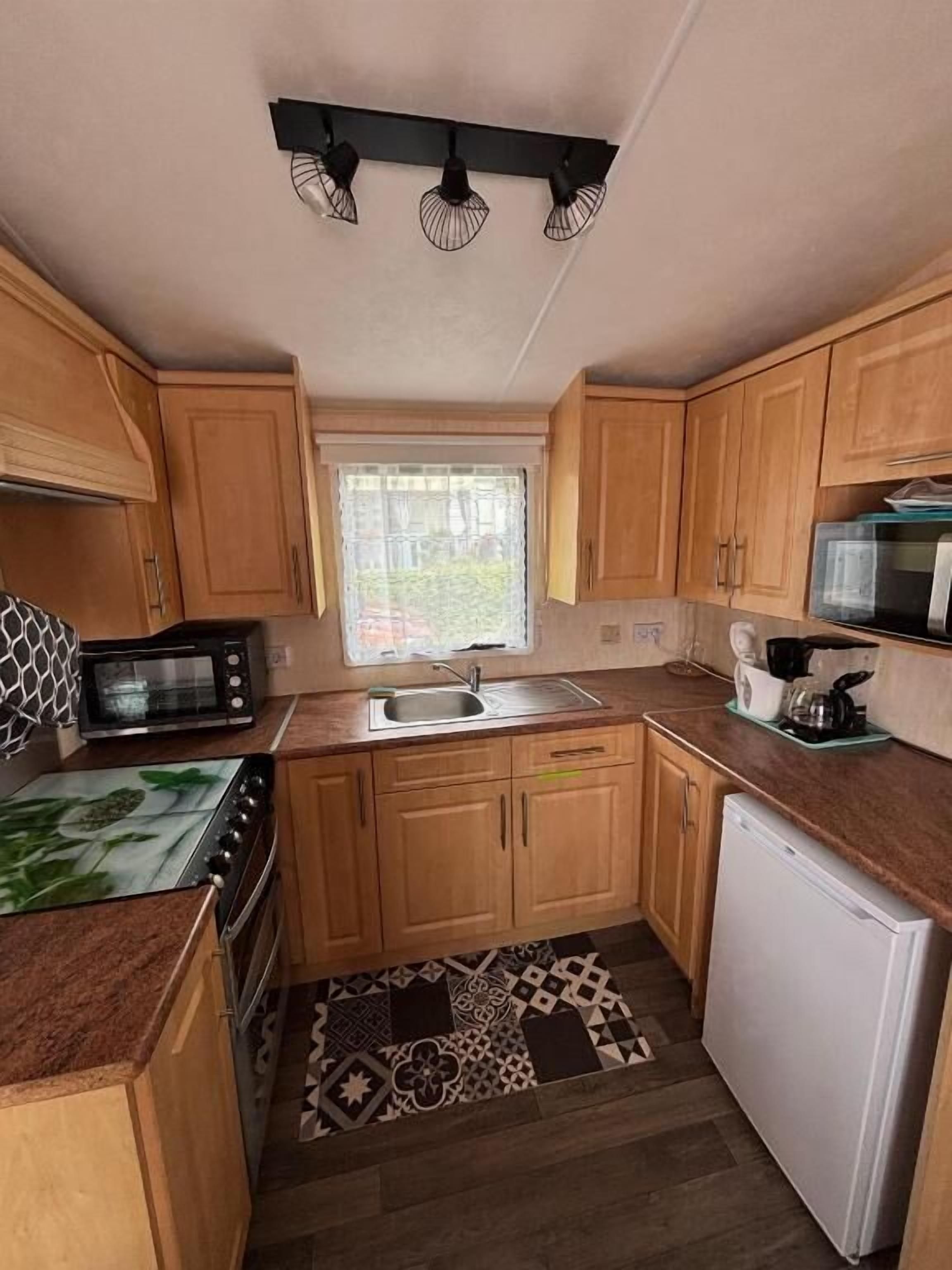 A compact kitchen with wooden cabinets, a microwave, a stove, a sink, and a refrigerator.