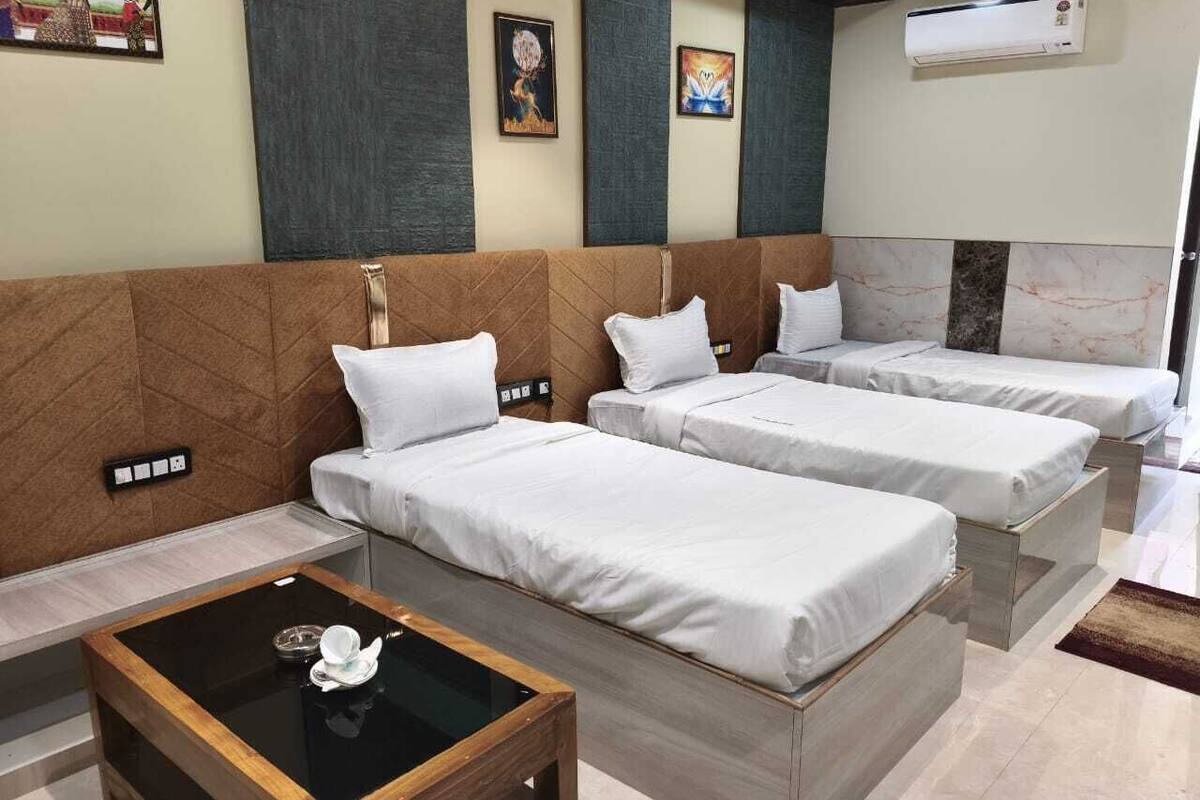 Habitación de hotel con dos camas individuales, una mesita pequeña y un aire acondicionado instalado en la pared.