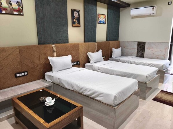 A hotel room with two single beds, a small table, and a wall-mounted air conditioner.