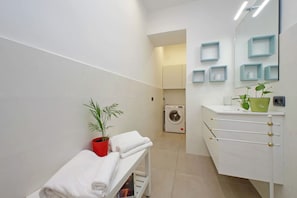 Ein modernes Badezimmer mit Sitzbank, Waschmaschine und Waschbecken mit Spiegel.