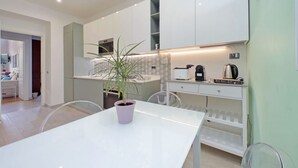 Una cucina moderna con mobili bianchi, un tavolo da pranzo con una pianta in vaso e una macchina per il caffè.