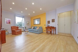 Ein geräumiges Wohnzimmer mit Holzboden, einem blauen Sofa, einem Holztisch und einem großen Spiegel an der Wand.
