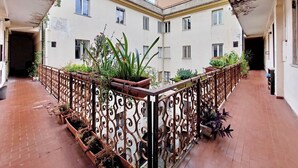 Un cortile con recinzione in ferro battuto, piante in vaso e pavimento piastrellato.
