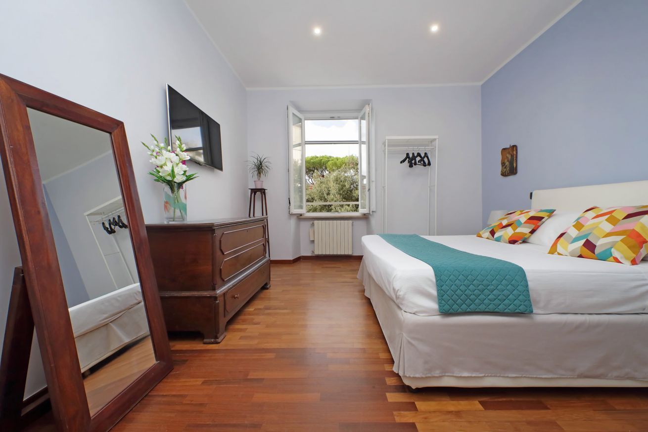 A bedroom with a bed, dresser, mirror, window, and a view of greenery outside.