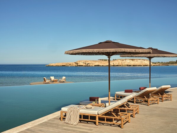 A poolside area with lounge chairs and umbrellas overlooking a calm sea.