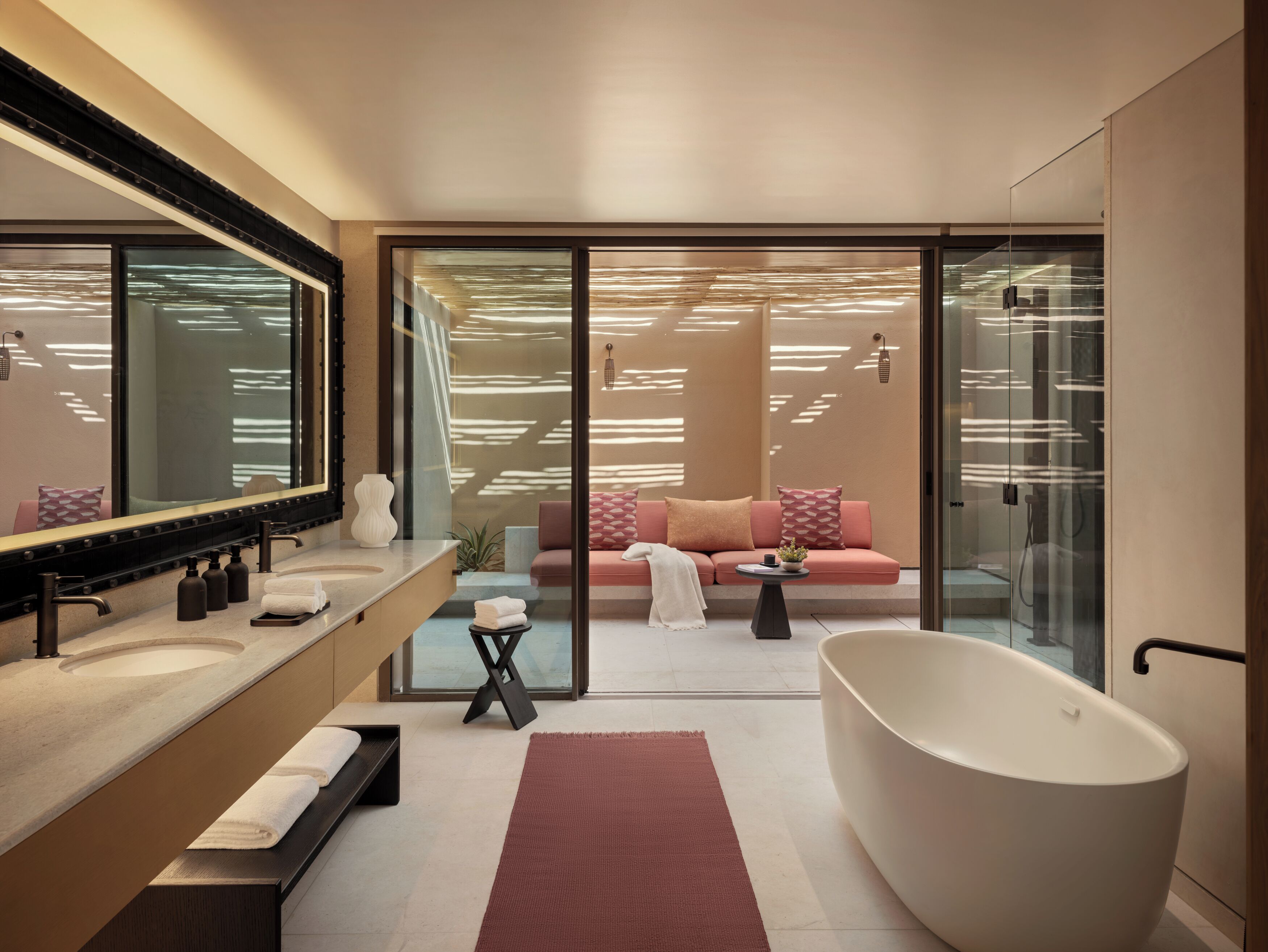 A modern bathroom with a freestanding bathtub, a large mirror, and a glass-enclosed seating area with a sofa.