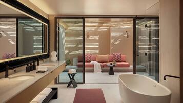 A modern bathroom with a freestanding bathtub, a large mirror, and a glass-enclosed seating area with a sofa.